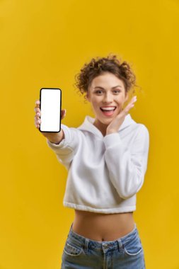 İçeride beyaz ekranlı akıllı telefon gösteren mutlu bulanık kız. Cep telefonunun boş ekranlı yakın görüntüsü, sevimli, bulanık bir kadın tarafından tutuluyor, turuncu stüdyo arka planında izole edilmiş. Aygıt kavramı.