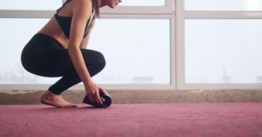 Sıska, spor takım elbiseli genç bir kadının yan görünüşü, evdeki kırmızı halıya menekşe yoga minderi sermesi. Güzel, esmer, at kuyruklu kız yoga yapıyor. Modern hayat kavramı.