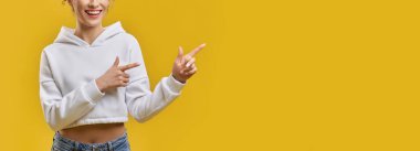 Kapalı alanda parmaklarıyla doğru yönü gösteren tanınmayan bir kız. Gülümseyen kadın görüntüsü, düzgün elleri olan, sarı stüdyo arka planında izole edilmiş, kopyalama alanı. El kol hareketi kavramı.