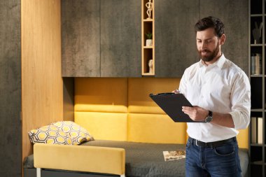 Mobilya fuarı merkezinde çalışırken esmer bir satıcı not alıyor. Mutluluktan sakallı müdürün tablete bakıp arka plandaki dolabın önünde duruşu. Çalışma alanı kavramı. 