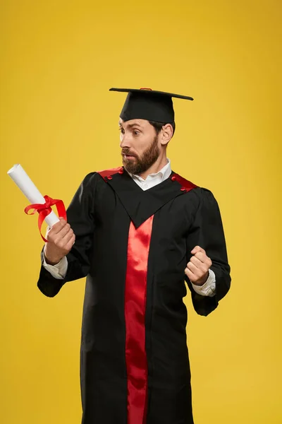 若いブルネットの男性立ちの正面図は 卒業証書を見て 高校を卒業したハンサムな男の子はショックを受けました 教育と知識の概念 — ストック写真