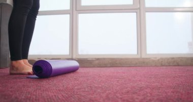 Spor takım elbiseli, ince, sportif bir kızın evinde menekşe yoga minderini sererken yakın plan. Güzel, genç bir bayan spor takım elbise giyiyor, yoga yapıyor. Yoga ve yeni çağ kavramı.
