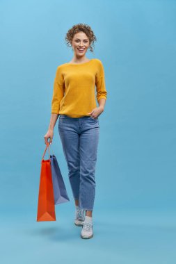 Paketleri elle tutan zayıf bir kızın ön görüntüsü. Genç, güzel bir bayan, ayakta, gülümsüyor, kameraya bakıyor, alışveriş yapıyor. Gençlik kavramı ve hayatın keyfi,