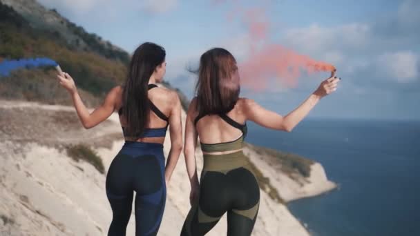 Jovens meninas esportistas ficar em um penhasco segurando bombas de fumaça coloridas — Vídeo de Stock