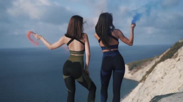 Jonge meisjes sportvrouwen staan op een klif met gekleurde rookbommen — Stockvideo