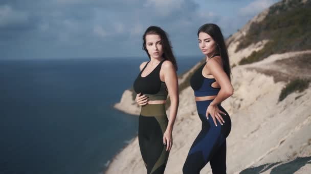 Slow motion two beautiful attractive athletic women posing on the edge of cliff — Stock Video