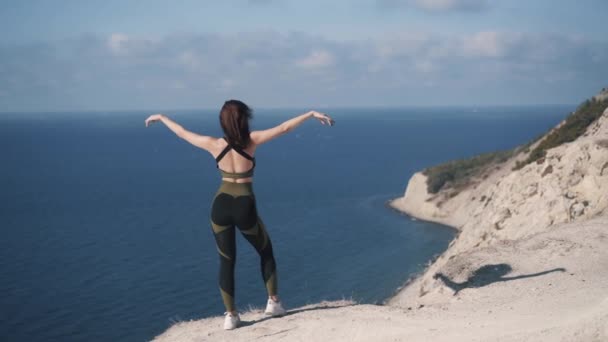 Jonge sportvrouw aan de rand van een klif en bewondert het uitzicht op zee — Stockvideo