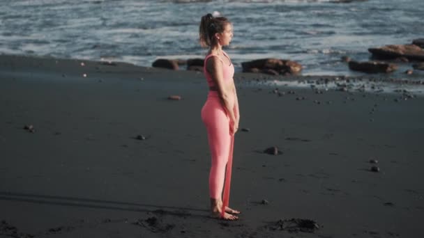 Side view gyönyörű fiatal nő csinál gyakorlatokat rugalmas szalag szabadban. — Stock videók