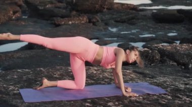 Güzel genç bir kadın plajda yoga minderi üzerinde egzersiz yapıyor..