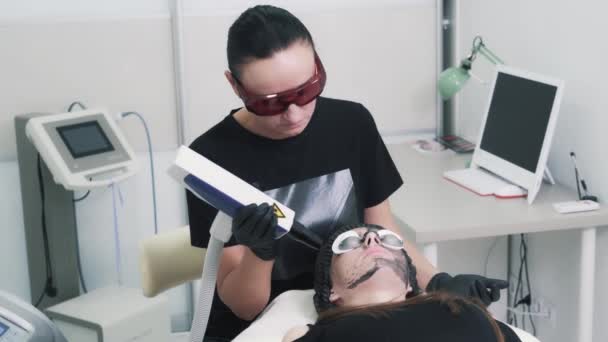 Kosmetolog dělá laserový uhlíkový peeling pro mladou bělošku. — Stock video