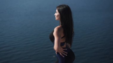 Kafkasyalı esmer kadın spor kıyafetleriyle deniz kenarında dinlenmeyi seviyor.