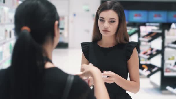 Vista frontal da jovem mulher conversando com o assistente de loja na loja de cosméticos. — Vídeo de Stock