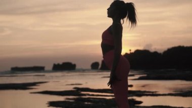 Sahilde jimnastik yapan beyaz bir kadının arkadan görünüşü..