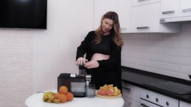 Hamile kadın elektrikli meyve sıkacağı kullanarak taze narenciye suyu yapıyor.
