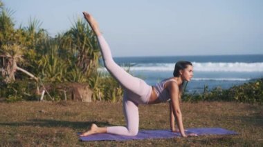 Deniz kıyısında egzersiz yapan ve eşek tekmesi atan atletik bir kadın.