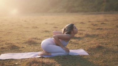 Paspasın üzerinde oturan ve bükülen bir kız. Isınmak ya da kasları kasmak için egzersizler yapmak. Gün batımında dışarıda antrenman yapan genç bir kadın.