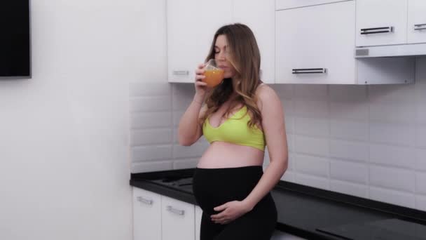 キッチンで新鮮なオレンジジュースを楽しむ妊婦さんの笑顔 妊娠中の健康と健康 食べる計画を維持する — ストック動画