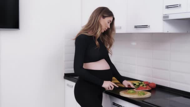 准妈妈在厨房里做饭 怀孕需要健康的饮食 所以女人做新鲜蔬菜沙拉和切鳄梨 — 图库视频影像