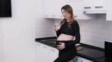 Müstakbel anne evdeki mutfakta bir bardak suyla bir yudum alıp karnını okşuyor. Hamilelik boyunca susuz kalmamak önemlidir. 