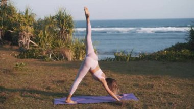 Esnek ve atletik kız deniz kenarında sıkı çalışıyor. Bacaklarını kaldırarak yere bakan genç bir kadın. Yaşam tarzı olarak spor ve spor