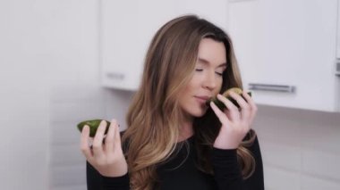 Avokado yarımları olan mutlu genç bir kadının ev portresi. Neşeli kız Keto diyeti için en sevdiği malzemeyi gösteriyor. Vejetaryen ve sağlıklı beslenme 