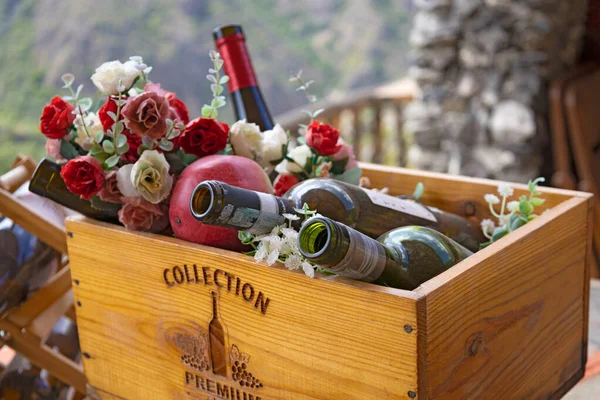 Wooden box with empty wine bottles, fruits and flowers, close up shot, shallow depth, bottles in focus, flowers blurred