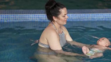 Anne, bebeğe havuzda yüzmeyi öğretiyor. Bebek ve anne havuzda yüzerken iyi eğlenceler..