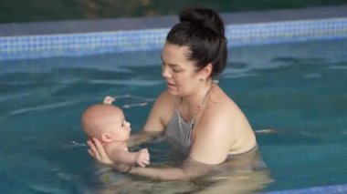 Anne, bebeğe havuzda yüzmeyi öğretiyor. Bebek ve anne havuzda yüzerken iyi eğlenceler..