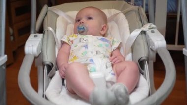 Elektronik salıncakta sallanan bir bebek, elektrikli sandalyede yatan şirin bir bebek. Çocuk gelişimi ve çocukluk.