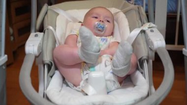 Elektronik salıncakta sallanan bir bebek, elektrikli sandalyede yatan şirin bir bebek. Çocuk gelişimi ve çocukluk.