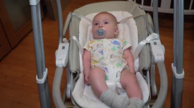 Elektronik salıncakta sallanan bir bebek, elektrikli sandalyede yatan şirin bir bebek. Çocuk gelişimi ve çocukluk.