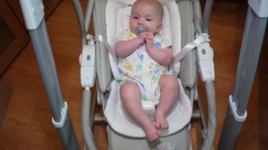 Elektronik salıncakta sallanan bir bebek, elektrikli sandalyede yatan şirin bir bebek. Çocuk gelişimi ve çocukluk.