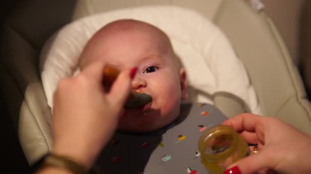 Mother giving food to baby boy, puree from spoon in highchair at home. Complementary infant feeding. — Stockvideo