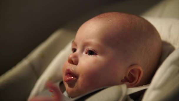 Moeder geeft eten aan baby jongen, puree van lepel in kinderstoel thuis. Aanvullende zuigelingenvoeding. — Stockvideo