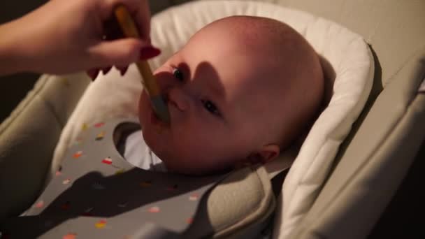 Мати дає їжу маленькому хлопчикові, пюре з ложки у високому кріслі вдома. Додаткове годування немовлят . — стокове відео