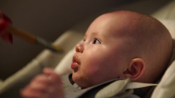 Madre dando comida al niño, puré de cuchara en silla alta en casa. Alimentación infantil complementaria. — Vídeos de Stock