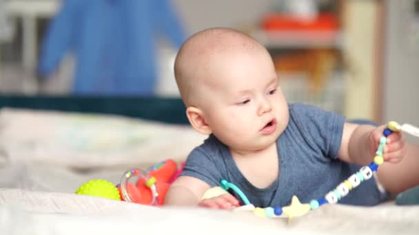 5 maanden oude actieve baby raakt speelgoed aan. Baby baby jongen spelen met het ontwikkelen van speelgoed liggend op de bank. — Stockvideo