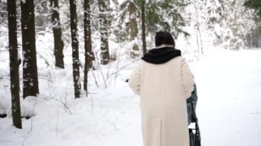 Genç anne kış ormanında bir bebek arabasıyla yürüyor..