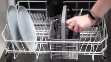 Kız bulaşık makinesine bardak, tabak ve çatal bıçak koyuyor.