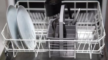Kız bulaşık makinesine bardak, tabak ve çatal bıçak koyuyor.