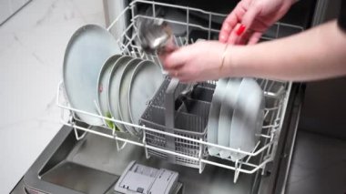 Kız bulaşık makinesine bardak, tabak ve çatal bıçak koyuyor.