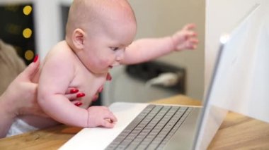 Young woman with toddler in arms typing on laptop, remote work with a baby at home.