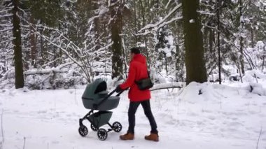 Dad with a baby stroller on a walk with a baby in the winter forest