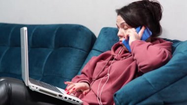 Kanepede oturan kulaklıklı ve dizüstü bilgisayarı olan bir kız. Evdeki koltukta uzaktan çalışma..