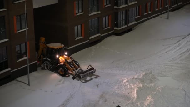 俄罗斯莫斯科- 2022年1月27日：特殊设备清理房屋院子里的积雪，推土机铲雪桶清除积雪. — 图库视频影像