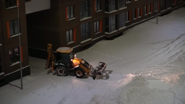 俄罗斯莫斯科- 2022年1月27日：特殊设备清理房屋院子里的积雪，推土机铲雪桶清除积雪. — 图库视频影像