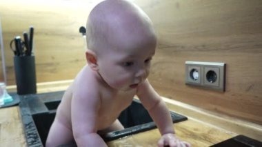 Mutfakta banyo yapan ve suyla oynayan bir bebek. Lavaboda musluktan suyla oynayan bebeğe yakın dur..
