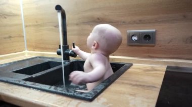 Mutfakta banyo yapan ve suyla oynayan bir bebek. Lavaboda musluktan suyla oynayan bebeğe yakın dur..