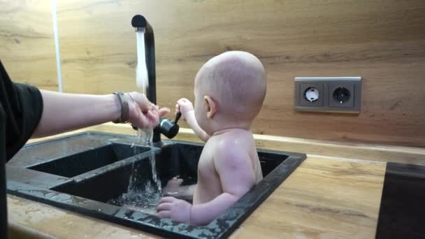 宝宝在厨房洗澡间洗澡和玩水 小宝宝用水龙头里的水在水槽里玩耍的特写镜头 — 图库视频影像