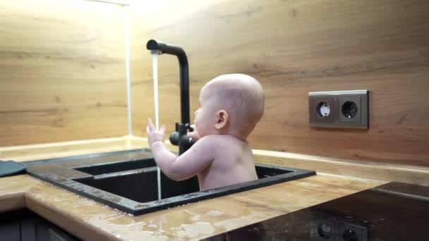 宝宝在厨房洗澡间洗澡和玩水 小宝宝用水龙头里的水在水槽里玩耍的特写镜头 — 图库视频影像